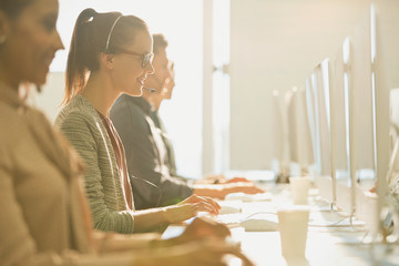 Female telemarketer wearing headset talking on telephone at computer in sunny office