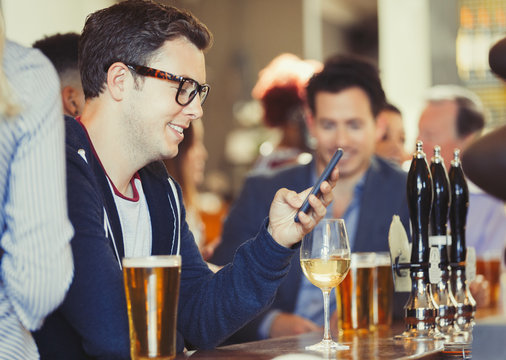 Smiling man texting with cell phone drinking wine at bar