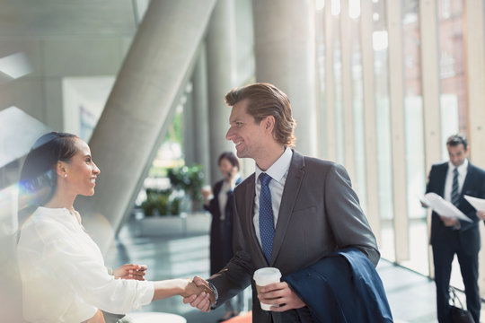 Businessman and businesswoman handshaking in sunny office lobby
