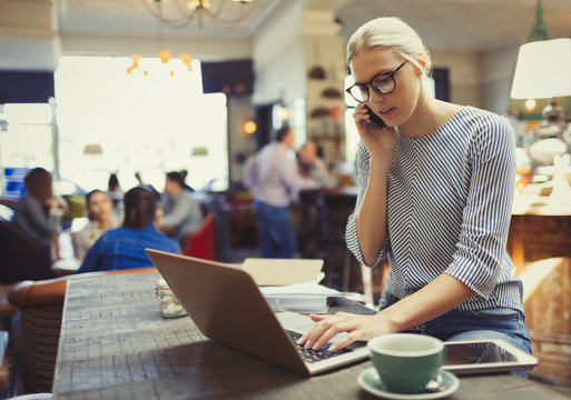 Creative businesswoman talking on cell phone and using laptop in cafe