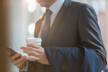 Close up businessman in suit with coffee texting with cell phone
