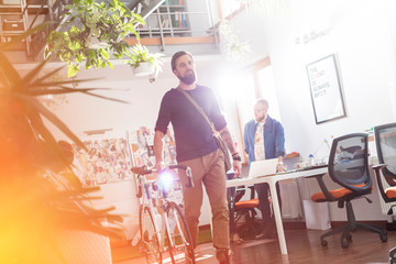Male design professional walking bicycle through office