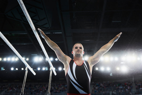 Male gymnast with arms raised next to parallel bars