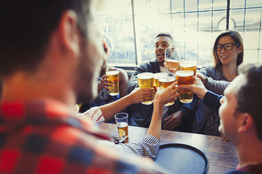 Friends celebrating, toasting beer glass at bar table