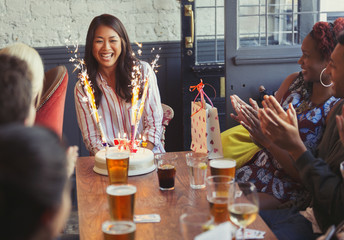 Friends clapping for happy woman fireworks birthday cake at restaurant table