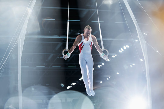 Focused male gymnast performing on gymnastics rings in arena