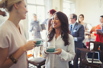 Smiling businesswomen drinking coffee networking at business conference