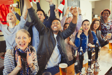 Enthusiastic sports fans cheering and watching game at bar