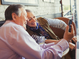 Smiling senior couple taking selfie with camera phone at cafe table