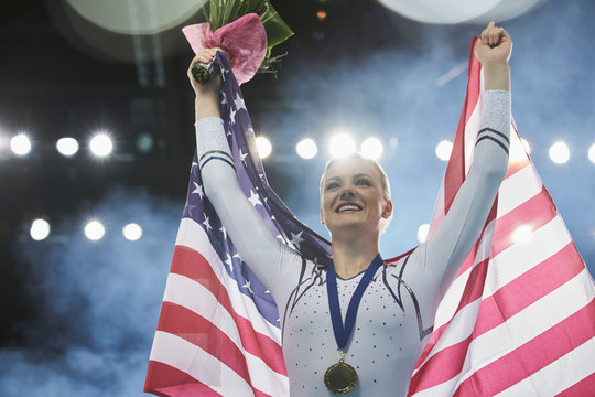 Enthusiastic female gymnast celebrating victory holding American flag on winners podium