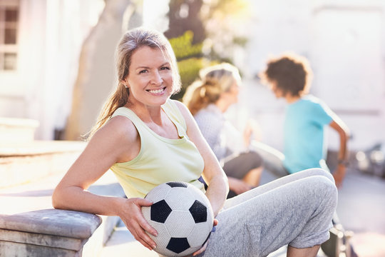 Portrait smiling woman holding soccer ball in sunny park