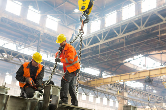 Steel workers fastening crane chain to steel in factory