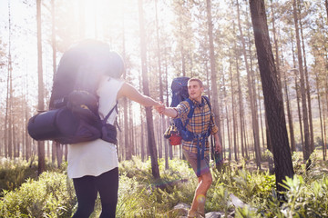 Young man helping girlfriend on hiking trail in sunny woods