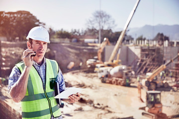 Construction worker foreman talking on walkie-talkie at sunny construction site