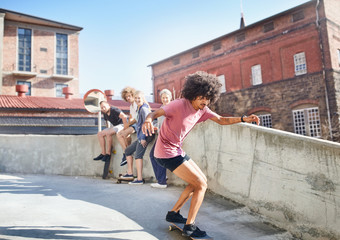 Friends watching man skateboarding on sunny rooftop