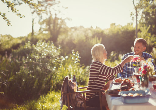 Couple toasting wine glasses at sunny garden party patio table