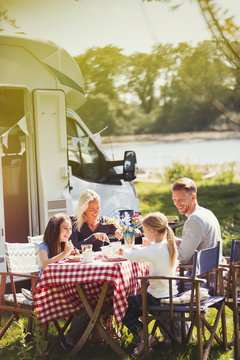 Family enjoying breakfast at table outside sunny motor home