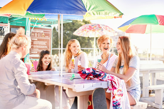 Happy women eating ice cream at sunny boardwalk picnic table