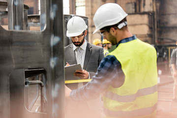 Manager with clipboard and steel worker with tape measure in factory