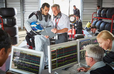 Manager formula one driver discussing telemetry diagnostics in repair garage