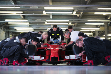 Pit crew preparing formula one race car and driver in repair garage