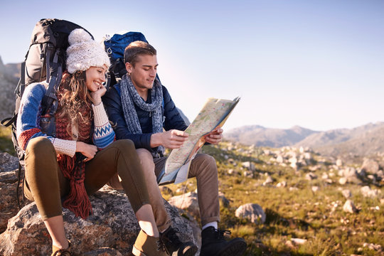 Young couple backpacks hiking, resting checking map on sunny rocks