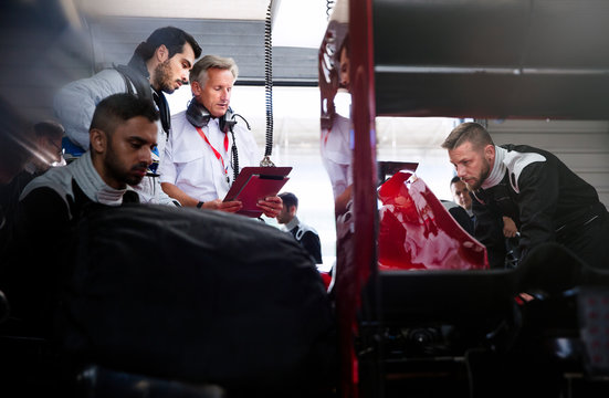 Manager driver talking behind pit crew working on race car in repair garage