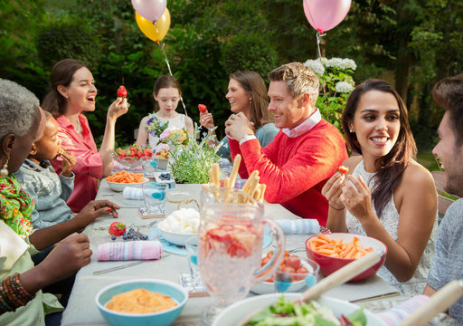 Family and friends enjoying birthday garden party at patio table