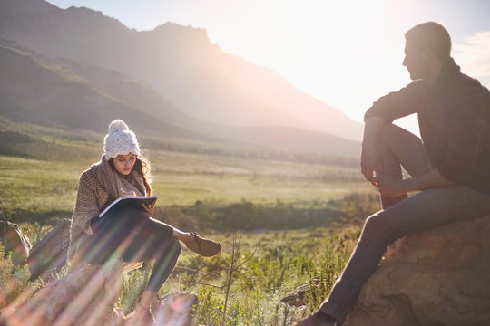 Young couple hiking, resting and writing in sunny remote field