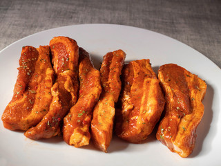 Korean style marinated pork belly slices, close up, on a white plate. Fresh meat preparation.