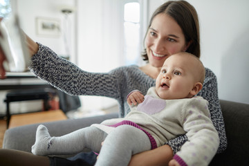 Smiling mother holding baby daughter taking selfie with camera phone