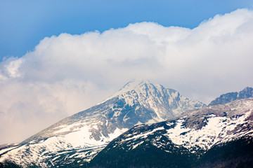 high tatras mountain ridge in springtime. snow capped rocky peaks in dramatic dappled sunlight beneath a clouds on a blue sky. place where earth meets sky concept