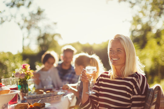 Smiling woman drinking wine at sunny garden party patio table - Powered by Adobe