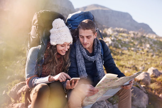 Young couple with backpacks hiking, resting checking map smart phone