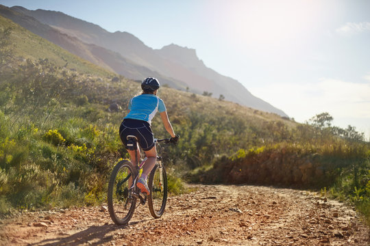 Young woman mountain biking on sunny, remote dirt road