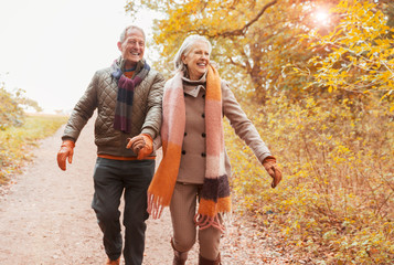 Smiling senior couple holding hands walking on path in autumn woods