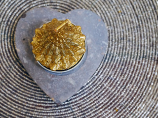 Golden candle on stone holder in a heart shape on a metal placeholder.