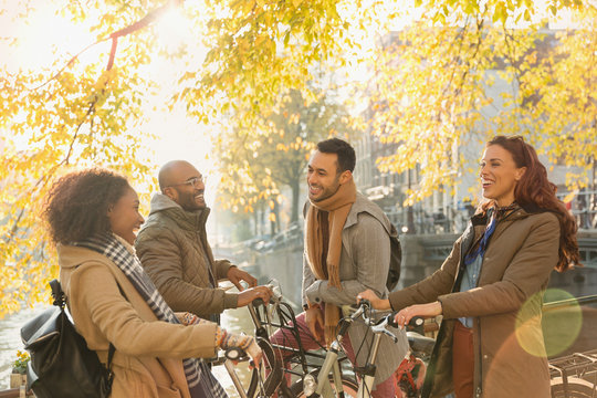 Smiling young couple friends bicycles talking under sunny autumn tree