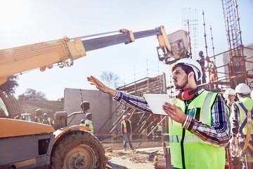 Construction worker foreman digital tablet guiding equipment at sunny construction site