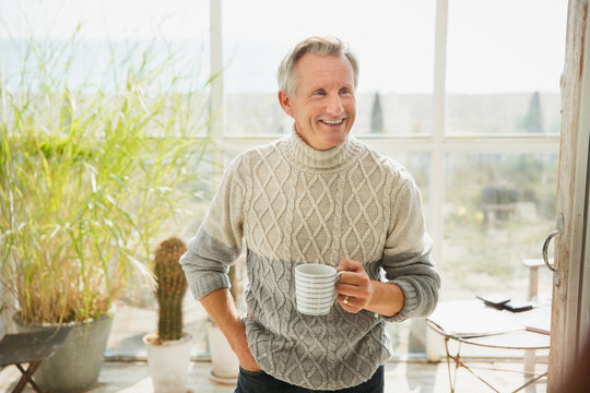 Smiling mature man drinking coffee on sunny beach house sun porch