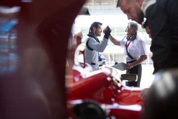 Manager and formula one race car driver high-fiving in repair garage