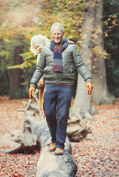 Senior couple walking on log in autumn woods