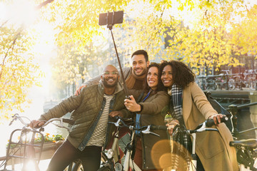 Smiling friends bicycle taking selfie selfie stick on urban bridge