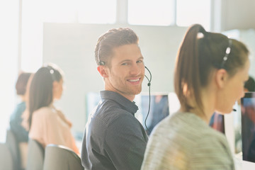 Portrait smiling male telemarketer wearing headset at computer in sunny office