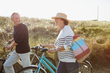Mature couple walking bicycles on sunny beach grass path