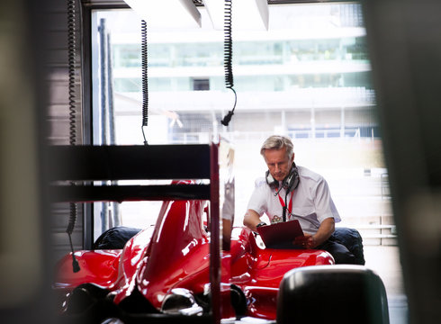 Manager with clipboard examining formula one race car in repair garage