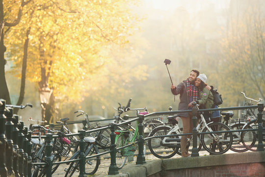 Young couple bicycles taking selfie selfie stick on autumn bridge, Amsterdam