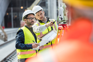 Male engineers using theodolite at construction site