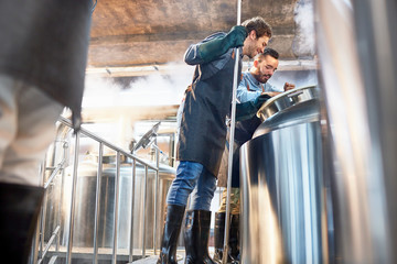Male brewers checking vat in brewery