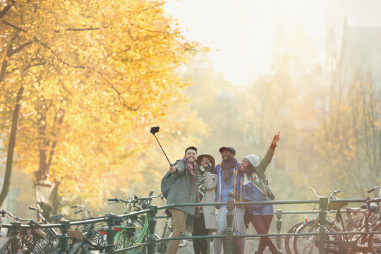 Playful young friends taking selfie selfie stick on urban autumn bridge, Amsterdam